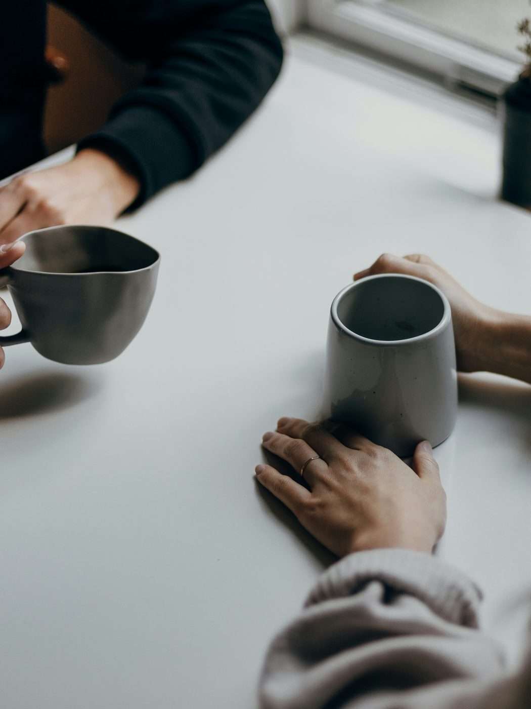 Zwei Menschen sitzen mit Tassen an einem hellen Tisch, im Gespräch