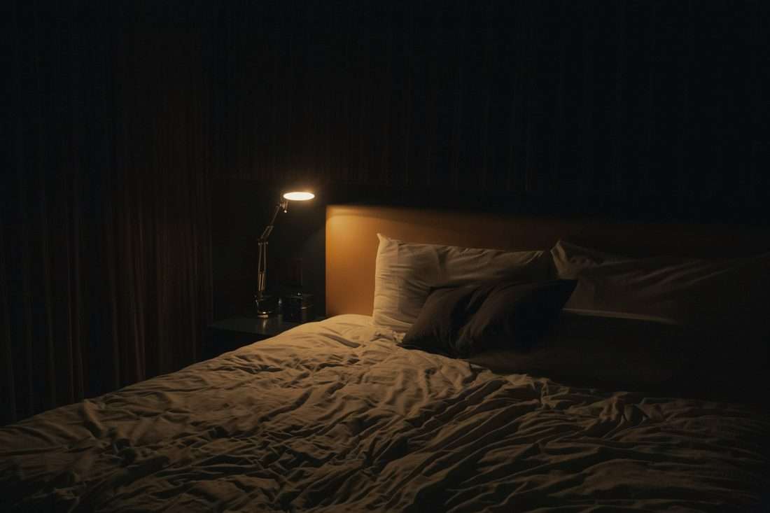 Ungemachtes Bett bei Nacht, die Nachttischlampe brennt noch